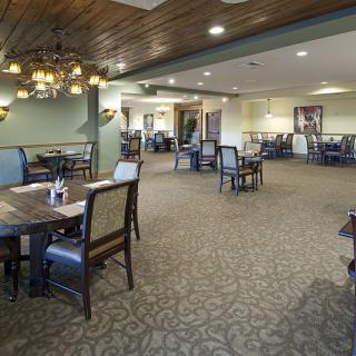 An empty restaurant dining area with neatly arranged tables and chairs, featuring a chandelier and carpeted flooring.