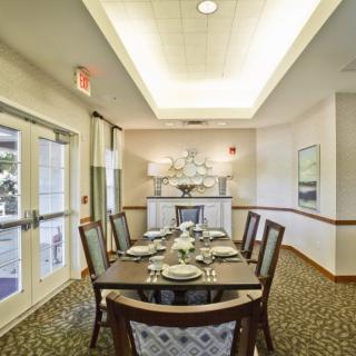 An elegantly set dining room with a rectangular table and upholstered chairs, under soft ceiling lighting.