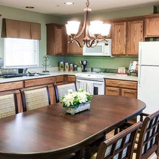 A cozy kitchen with a wooden dining table and matching chairs, featuring warm cabinets, a chandelier above, and essential appliances.