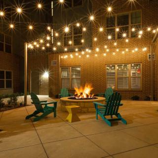 A cozy outdoor patio with string lights and a central fire pit surrounded by colorful chairs.