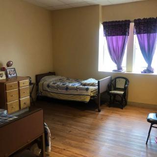 A cozy bedroom with a single bed and purple curtains on the windows.