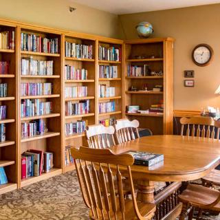 A cozy library reading room with bookshelves, a wooden table, and chairs.