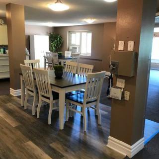 A cozy dining room setup with a wooden table and chairs, featuring wood flooring and ample natural light.