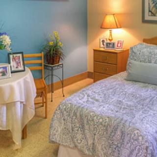 A cozy bedroom with a neatly made bed, a bedside table lamp, and decorative elements including plants and photo frames.