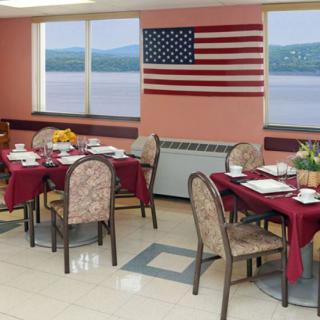 A dining room with tables set for a meal, featuring an American flag and large windows overlooking a scenic view.