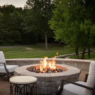 A cozy outdoor setting featuring a fire pit surrounded by comfortable seating, overlooking a lush garden.