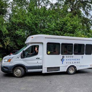 A white transportation van parked in a green outdoor setting.