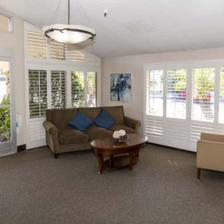 A cozy living room with a sofa, armchair, coffee table, and large windows with shutters.
