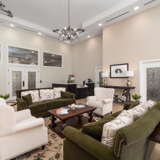 A spacious and elegantly designed living room with plush green sofas, a central coffee table, and sophisticated lighting.