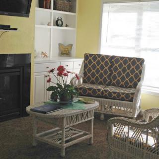 A cozy living room with a patterned chair and a wicker coffee table, accompanied by a fireplace and a bookshelf.