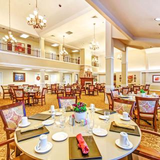 An elegant dining room with neatly arranged tables and chairs, featuring chandeliers and warm lighting.