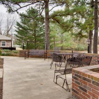 A peaceful outdoor patio area with tables and chairs surrounded by trees and brick walls.