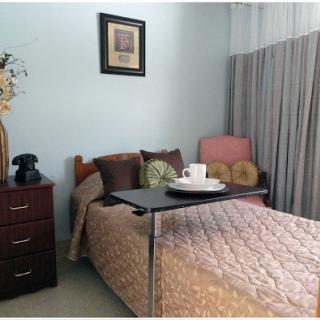 A cozy and well-decorated bedroom featuring a neatly made bed, a nightstand with a phone, and a small table set for tea.
