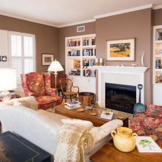 A cozy living room featuring a fireplace, bookshelves, and a mix of armchairs and sofa for seating.