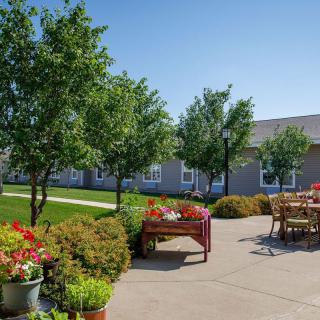 A sunny outdoor patio with tables and chairs surrounded by trees and vibrant flowers.