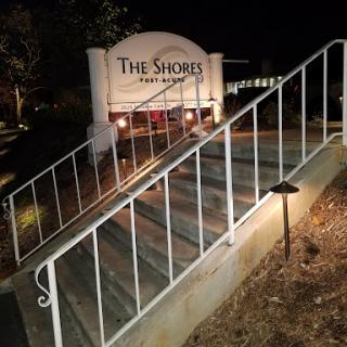 A view of 'The Shores' entrance at night, featuring illuminated stairs and a prominent sign.