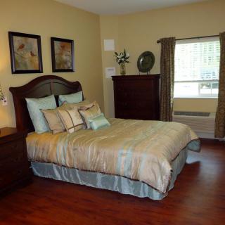 A cozy bedroom with a neatly made bed, artwork on the walls, and wooden flooring.