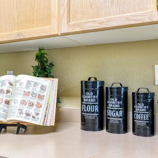 A kitchen countertop featuring black canisters labeled for flour, sugar, and coffee, alongside an open recipe book.
