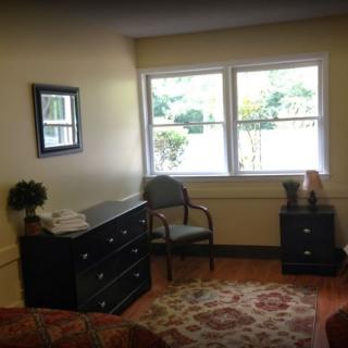 A cozy room with a dresser, chair, and large window.
