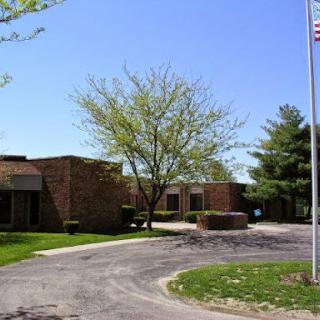 A view of a brick building surrounded by greenery and a flag flying in the breeze.
