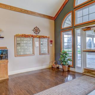 A welcoming lobby with wood floors, mailboxes, and indoor plants near a large window entrance.