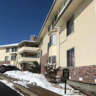 A multi-story apartment building with snow on the ground, set against a clear blue sky.