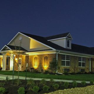 A well-lit suburban house at night with a brick exterior and landscaped front yard.