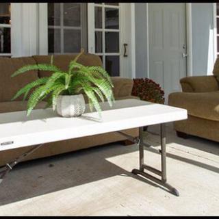 An outdoor patio area with a sofa and armchair, featuring a white coffee table adorned with a potted fern.