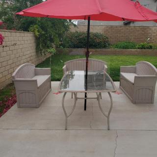 An outdoor patio setup with a red umbrella, glass table, and two chairs in a garden setting.