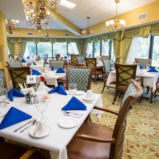 An elegant restaurant dining room with tables set with blue napkins and chandeliers overhead.