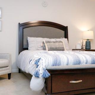 A cozy bedroom featuring a neatly made bed with striped bedding, a nightstand with a lamp, and an armchair.