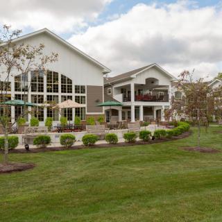 A spacious building with large windows surrounded by a well-maintained lawn and trees under a partly cloudy sky.
