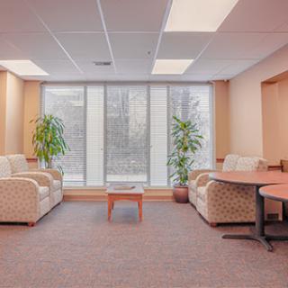 A cozy office waiting area featuring comfortable sofas, a central table, and potted plants.