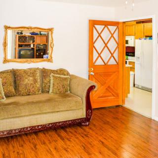A cozy living room with a plush sofa, elegant mirror, and a view into the kitchen through an open wooden door.