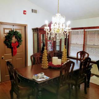 A warmly decorated dining room with a chandelier, featuring holiday accents such as a wreath and festive table centerpiece.