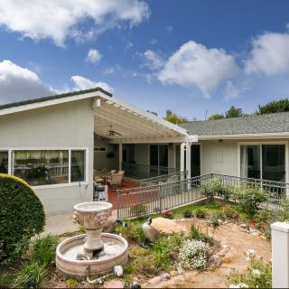 A beautiful house with a garden featuring a fountain and a covered porch under a partly cloudy sky.