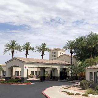 A building entrance with palm trees lining the driveway under a cloudy sky.