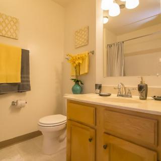 A cozy bathroom with yellow accents, featuring a sink, mirror, and toilet.