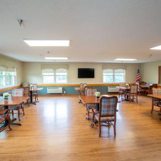 A spacious dining area featuring wooden tables and chairs, with ample natural light from large windows.