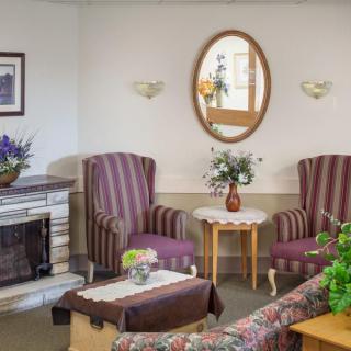 A cozy living room with striped armchairs, a decorative mirror, and floral arrangements.