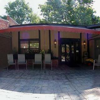 A patio area with several chairs in front of a building entrance, surrounded by trees.