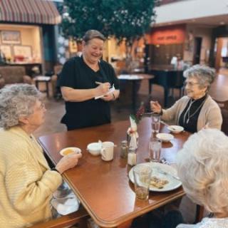 A waitress taking an order from a group of seniors enjoying a meal together.