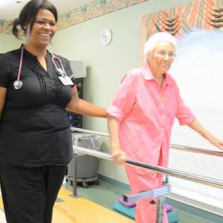A nurse assists an elderly woman during a physical therapy session.