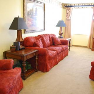 A cozy living room with red sofas, side tables, and decorative lamps under warm natural lighting.
