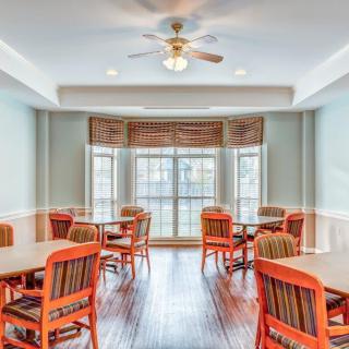 A bright dining area with orange chairs and tables, featuring large windows and a ceiling fan.