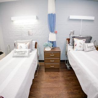 A well-organized patient room featuring two beds, each with white linens and decorative pillows.