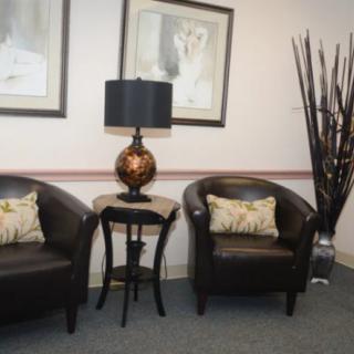 A waiting room with two leather chairs, a lamp on a small table, and framed artwork on the walls.