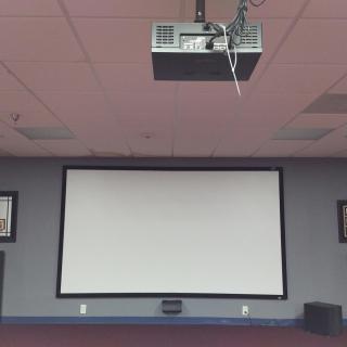 A ceiling-mounted projector facing a large presentation screen in a conference room.