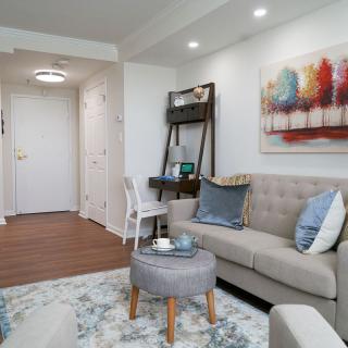 A modern living room featuring a comfortable sofa, abstract wall art, and a small desk along with wooden flooring.