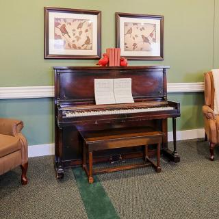 A cozy room featuring a vintage upright piano with sheet music and two armchairs, adorned with framed artwork above.